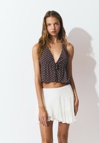 Top halter de lunares marrones con un lazo en la parte delantera, combinado con una mini falda blanca de capas con un dobladillo ondulado. Textura de tela suave.