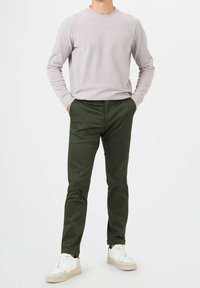 Ljusgrå crew-neck tröja, slim-fit mörkgröna byxor och vita sneakers med beige accenter. Slät textur och avslappnad design.