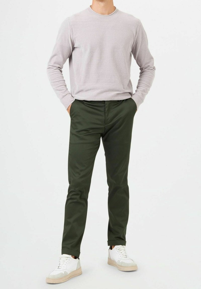 Ljusgrå crew-neck tröja, slim-fit mörkgröna byxor och vita sneakers med beige accenter. Slät textur och avslappnad design.