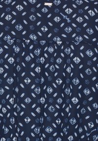 Tessuto navy con motivi geometrici bianchi e blu, caratterizzato da piccoli quadrati, cerchi e un'etichetta "Pepe Jeans" incorporata.