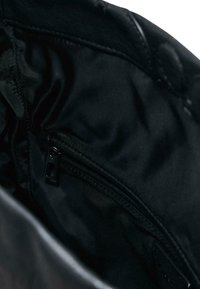 Intérieur en tissu noir d'un sac avec une petite poche zippée et des détails de couture visibles.
