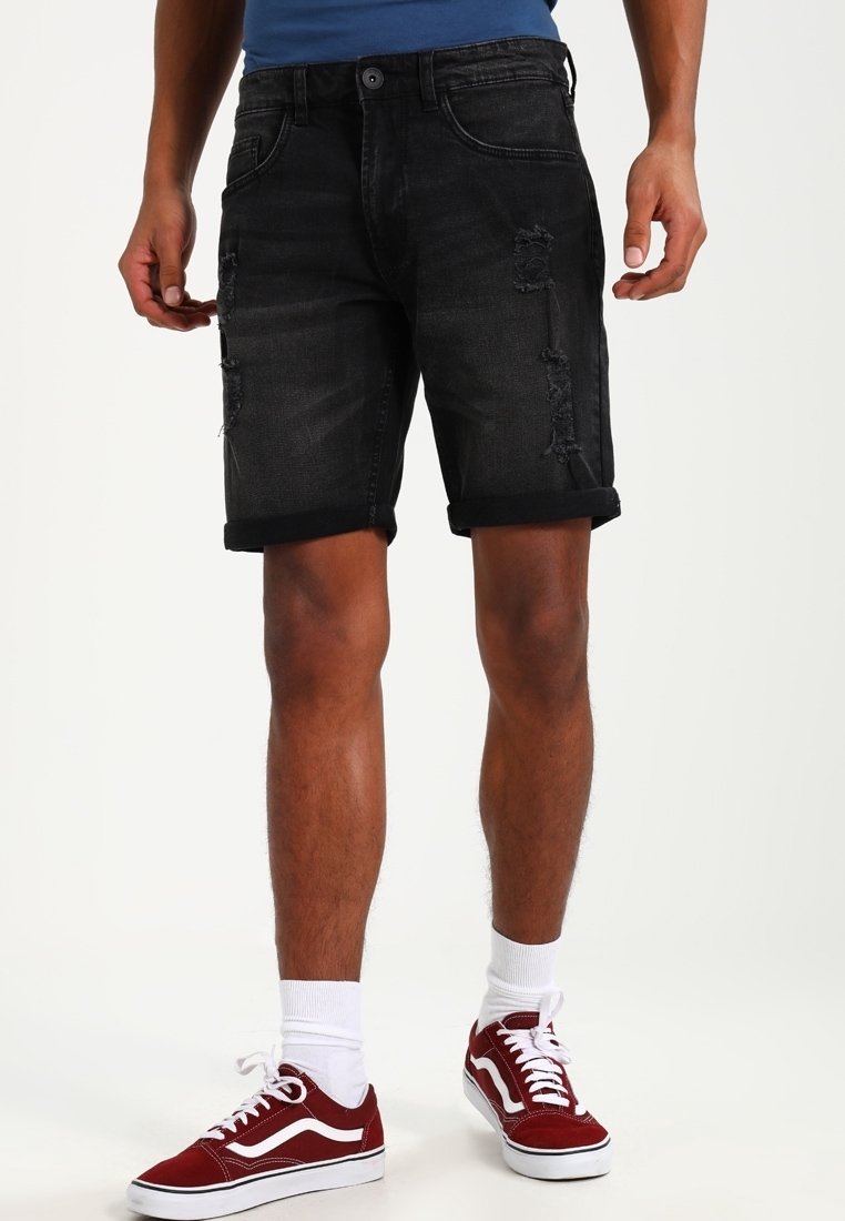 Shorts en denim noir avec des détails déchirés, des manches retroussées et un design à cinq poches. Associés à des baskets rouge, blanche et noire.