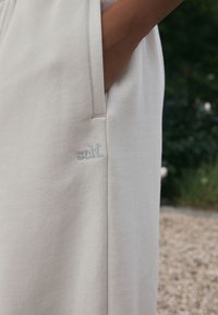 Šviesiai pilka, minkšta medvilninė suknelė turi šoninę kišenę ir siuvinėtą „self“ detalę. Lygi tekstūra su paprastu, moderniu dizainu.
