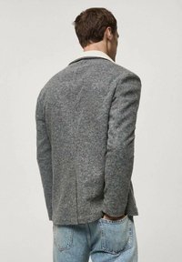 Gray wool blazer with notch lapel, single back vent, and structured shoulders, paired with light blue denim jeans.
