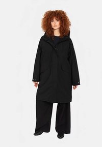 Schwarzer langer Mantel mit Kapuze, Reißverschluss vorne, zwei Seitentaschen und lockerer Passform. Hergestellt aus glattem, wetterbeständigem Stoff.