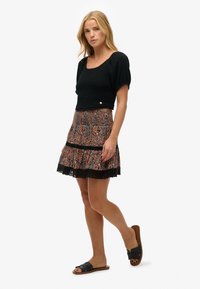 Sort smocked crop top med korte puffærmer, parret med en mønstret mini nederdel med orange, blå og sort snit.