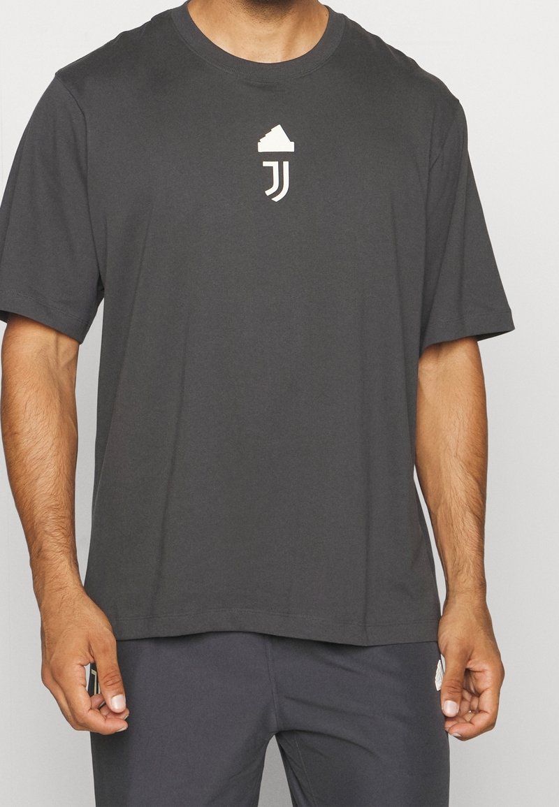 Homme portant un t-shirt gris foncé à manches courtes avec un logo blanc centré sur la poitrine et un pantalon gris foncé assorti.