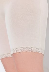 Shorts en coton beige à la texture lisse, présentant une délicate bordure en dentelle à l'ourlet, offrant une coupe ajustée et une élégance subtile.