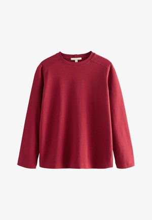 Punane pikkade varrukatega puuvillane ümmarguse kaelusega dressipluus ribatud kaelaava ja mansettidega. Sile tekstuur, lõdvestatud lõige ja minimaalne disain ilma kaunistusteta.