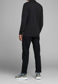 Svart långärmad pikétröja, i kombination med mörka byxor och skor med en blandning av grå, blå och beige accenter. Enkel design utan synliga mönster.