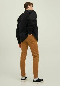 Black button-up shirt, tan chinos, and black sneakers with white accents; showing a relaxed fit and smooth textures from the back.