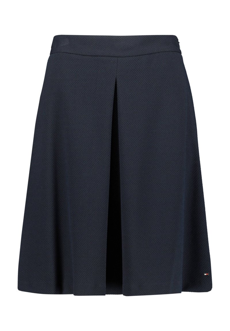 Tummansininen polviin asti ulottuva hame, jossa on edessä keskellä laskos ja hienovarainen tekstiilikuosi, pieni logo helman oikealla puolella.