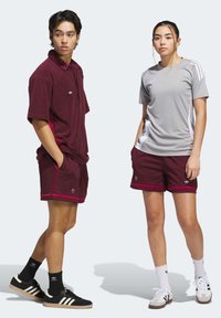 Red and gray athletic outfits, including a short-sleeve polo, shorts, and sneakers with contrasting stripes and branded accents.