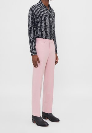 Zwarte gestreepte blouse met wit golvend patroon, gecombineerd met roze gepaste broek en zwarte leren dress boots. Geen zichtbare accessoires.