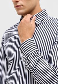 Camicetta da uomo a righe bianche e nere con colletto e polsini button-down. Presenta righe verticali di spessore uniforme con una superficie del tessuto liscia.