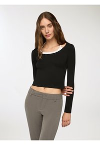 Top nero a maniche lunghe cropped con collo rotondo bianco, abbinato a pantaloni grigi slim, che mostrano una texture di tessuto liscia e una vestibilità aderente.