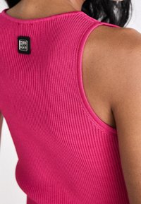 Tætsiddende ærmeløs top i ribstrikstof, i en livlig pink farve, med et sort mærke på bagsiden nær halsudskæringen.