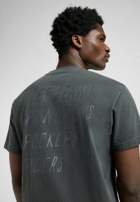 Camiseta de algodón gris con un gran texto sutil en la parte trasera. Diseño de mangas cortas y cuello redondo con una textura suave.