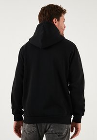 Černá mikina s kapucí, žebrovanými manžetami a lemem. Vyrobená z měkké látky, má volný střih a jednoduchý design.