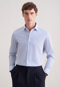 Camicia a righe azzurro chiaro con colletto button-down e maniche lunghe, realizzata in tessuto liscio. Abbinata a pantaloni scuri.