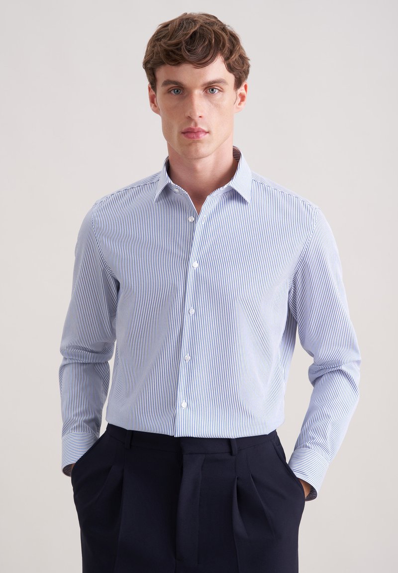 Camicia a righe azzurro chiaro con colletto button-down e maniche lunghe, realizzata in tessuto liscio. Abbinata a pantaloni scuri.