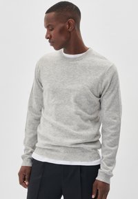 Svijetlosivi pulover s okruglim izrezom, izrađen od mekog materijala. Ima rebrasti rub i manžete, nosi se preko bijele košulje. Jednostavan dizajn.