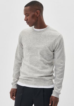 Hellgrauer, Rundhals-Pullover aus einem weichen Material. Verfügt über einen gerippten Saum und Bündchen, über einem weißen Hemd getragen. Einfaches Design.
