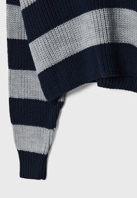 Neulepaita, jossa on tummansiniset ja vaaleanharmaat vaakaraidat, resorit hihansuissa ja ylipitkä malli, jossa on teksturoitu kangas.