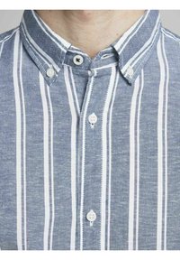 Blårandig skjorta med knappar och krage, med vita vertikala ränder och två vita knappar vid knäppningen.