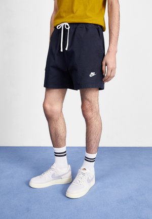 Granatowe szorty z bawełny z elastycznym pasem i białym sznurkiem do regulacji. Z przodu mały biały logotyp Nike przy dolnym brzegu.