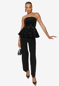 Melnā strapless peplum top ar pērlītēm, apvienots ar melniem taisniem biksēm un smailiem zābakiem. Modelis tur nelielu melnu somiņu.
