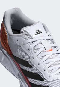 Witte sportschoen met een gestructureerd mesh bovenwerk, zwarte en rode accenten van synthetisch leer en een gevoerde kraag voor comfort.