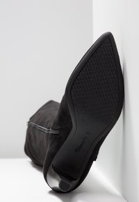 Schwarze Wildleder-Stiefelette mit einem Reißverschlussdetail, ausgestattet mit einem konischen Absatz und einer strukturierten Gummi-Außensohle. Größe 37.