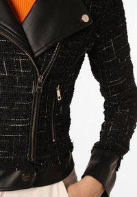 Schwarze Tweed-Jacke mit Lederelementen, weitem Kragen und Reißverschlusstaschen. Kontrastierende Texturen mit einer modernen, strukturierten Passform.