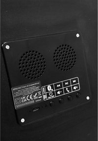 Svart elektroniskt panel med två runda högtalargrillar, kontrollknappar, en USB-C-port och en produktetikett med överensstämmelsemärken.
