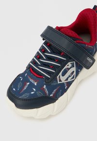 Granatowe buty sportowe z materiałową cholewką w wzory z czerwonymi i białymi liśćmi. Wyposażone w pasek na rzep oraz gumową podeszwę.