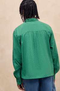 Grønternet langærmet skjorte med knaplukket krave og plisseret ryg, kombineret med blå jeans. Tekstureret stof med afslappet pasform.