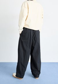 Svarta vida byxor i lätt material, med hög midja och två bakfickor. Kombinerade med en krämfärgad oversized sweatshirt.