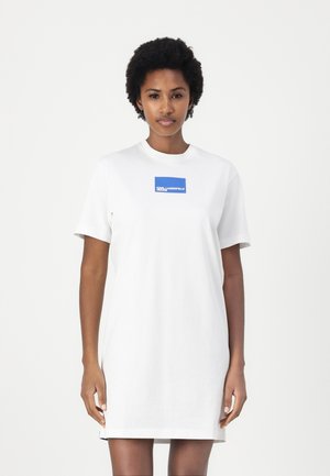 Hvit bomulls t-skjortekjole med korte ermer, med en blå rektangulær logomerke i midten. Enkel, løstsittende design.