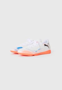 Chaussures de soccer en salle Puma blanches avec semelles orange, design dégradé bleu et orange, et logo Puma noir sur le côté.