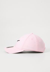 Lyserød baseballkasket med sort logo foran og buet skygge, vist fra siden på en ensfarvet hvid baggrund.