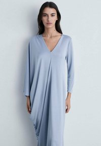 Long-sleeve, V-neck dress in soft, light blue fabric with draped design and relaxed fit, flowing gently from the shoulders.