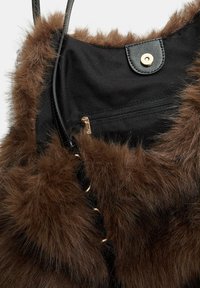 Une fourrure synthétique brune orne le dessus d'un sac en tissu noir, doté d'une fermeture à bouton-pression doré et d'une poche zippée pour le rangement.