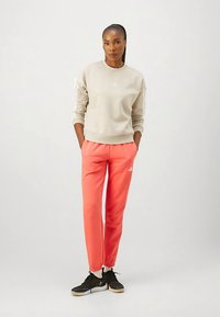 Ljusgrå sweatshirt med ribbade manschetter och rundad hals, ihop med ljusrosa joggingsbyxor med sidofickor och vita logodetaljer. Svarta sneakers.