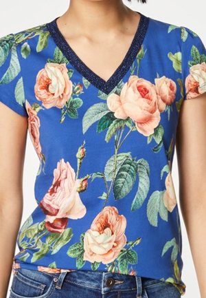 Camiseta azul de cuello en V con grandes rosas rosas y durazno y hojas verdes, combinada con vaqueros azules de mezclilla.
