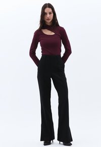 Burgundy långärmad topp med utskuret detalj, matchad med hög midja svarta utsvängda byxor. Slät textur och skräddarsydd passform.