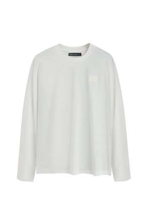 Camiseta blanca de manga larga hecha de algodón suave, con un escote redondo y un parche de logo cuadrado texturizado en el lado izquierdo del pecho.