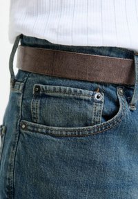 Kék mosású farmernadrág, texturált felülettel, világosbarna bőr övvel. Zsebek fémbetétekkel.