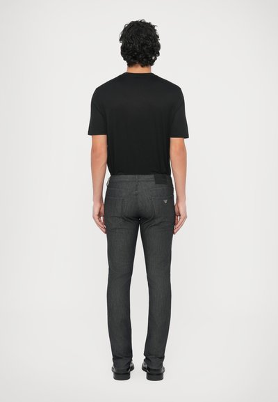 Črna majica s kratkimi rokavi v kombinaciji s temno sivimi ozkimi kavbojkami. Zadnji pogled prikazuje žepe in subtilen logotip na pasu.