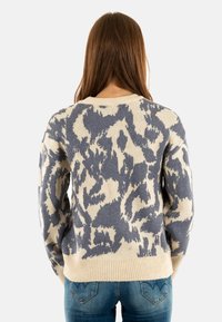Pull créme avec un motif abstrait bleu, encolure et poignets côtelés, coupe décontractée, fabriqué à partir d'un matériau en maille doux.